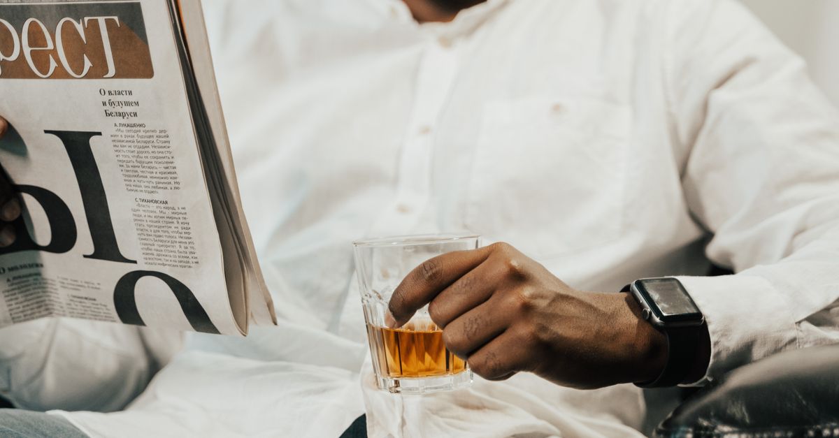 Man reading a newspaper while holding a drink, showcasing leisure and modern lifestyle.